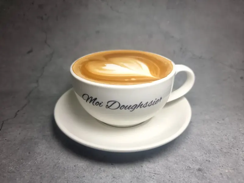 A freshly made latte in a branded Moi Doughssier cup with latte art, served at the café